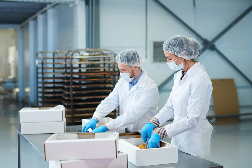 A man and a woman packaging food in a manufacturing plant